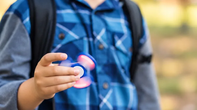 A boy in a checked shirt and backpack holding a spinning fidget spinner
