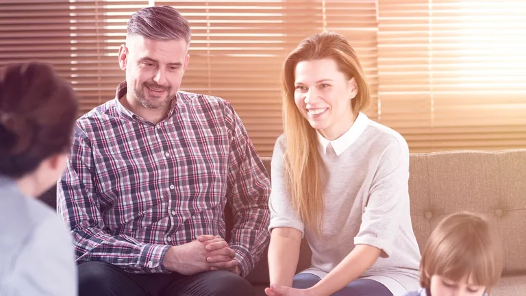 Two parents sitting together on a sofa, listening, with their young child beside them