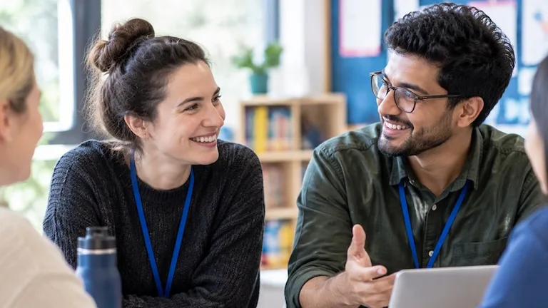 Two colleagues wearing lanyards talking and smiling at a work table